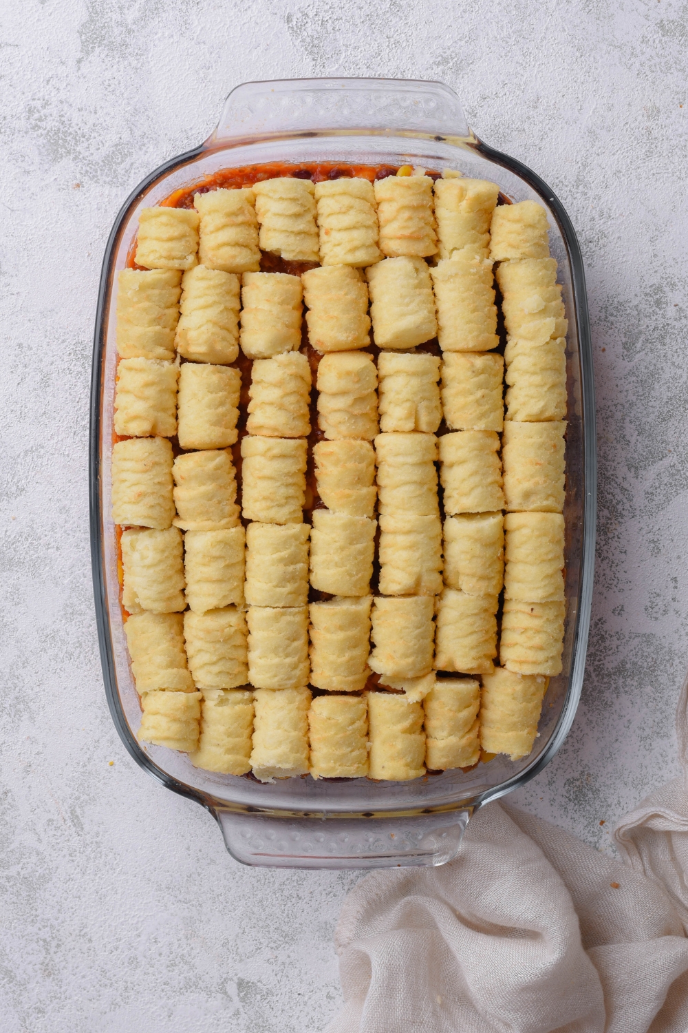 Tater tots arranged on a casserole filling in a baking dish on top of a grey counter.