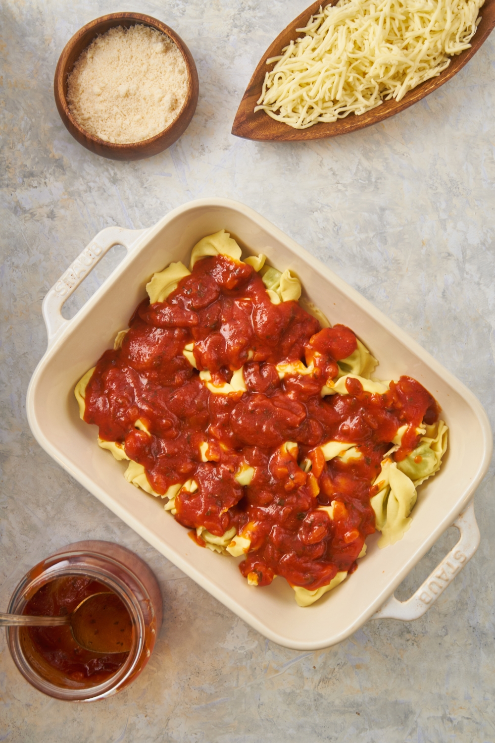Sauce on top of tortellini in a baking dish on top of a white counter.