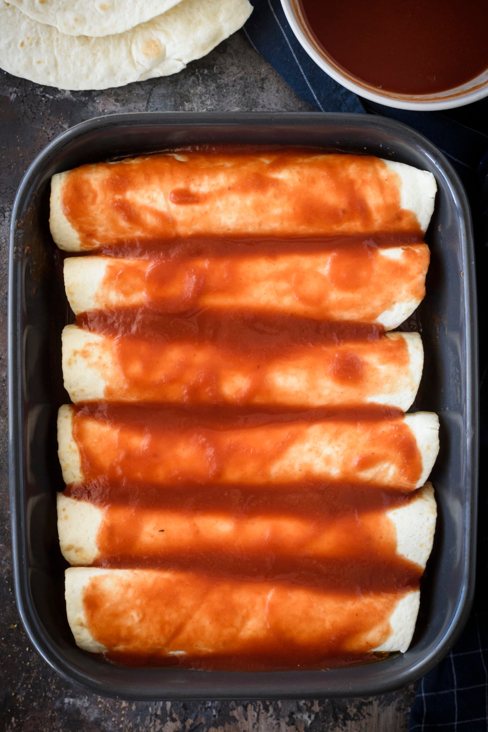 A casserole dish with wrapped enchiladas topped with enchilada sauce.