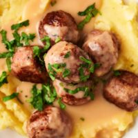 An IKEA meatball on top of four meatballs on top of gravy on mashed potatoes on a white plate.