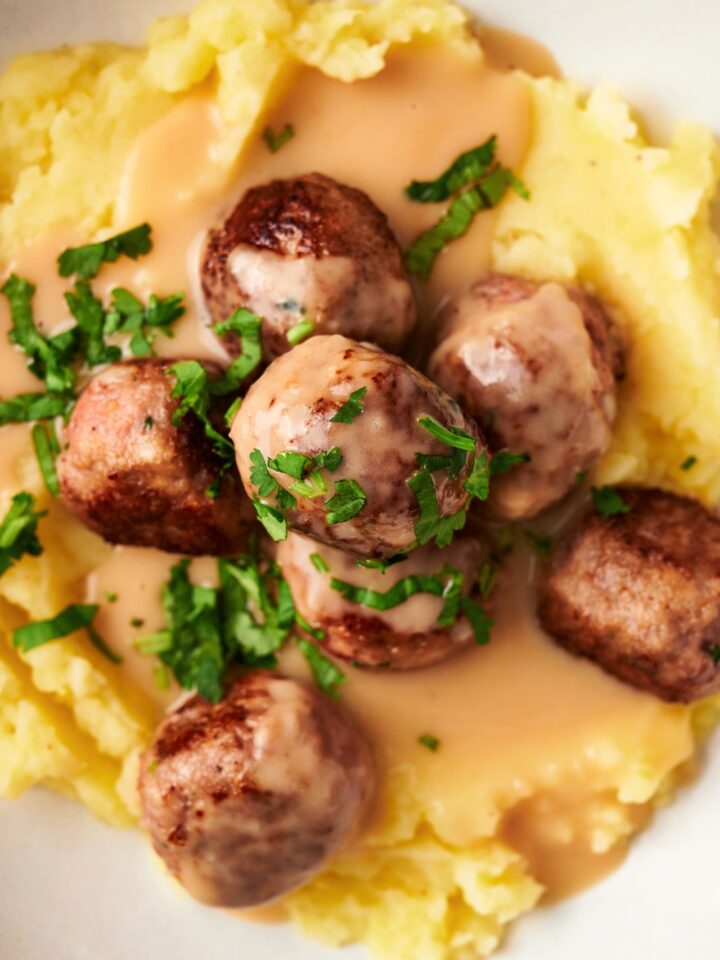 An IKEA meatball on top of four meatballs on top of gravy on mashed potatoes on a white plate.