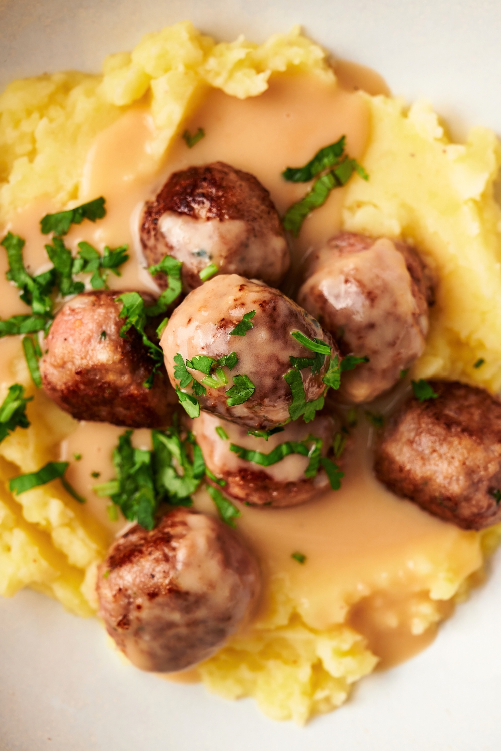 An IKEA meatball on top of four meatballs on top of gravy on mashed potatoes on a white plate.