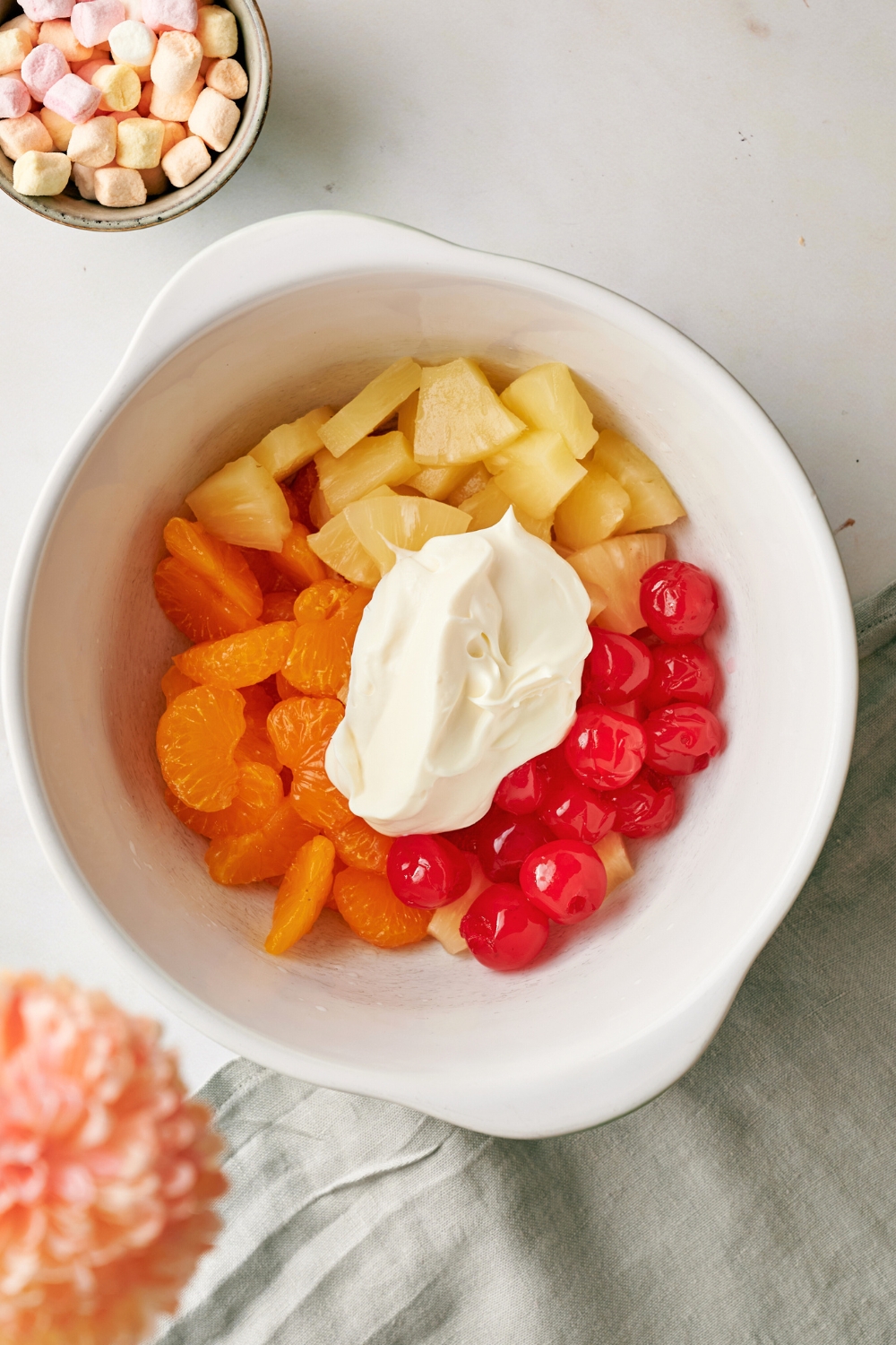 A scoop of Cool Whip on top of mandarin oranges, pineapple chunks, and maraschino cherries in a bowl.