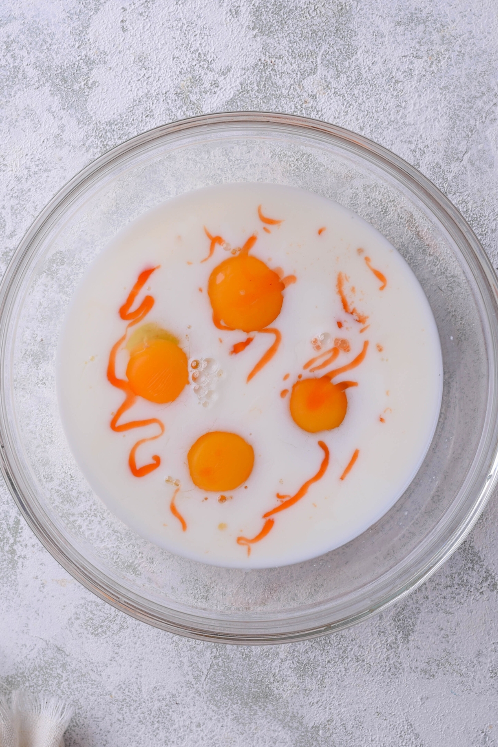 A mixing bowl with milk, hot sauce, and eggs.