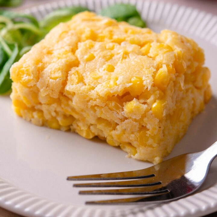 A slice of Jiffy corn casserole on a white plate with a fork on it.