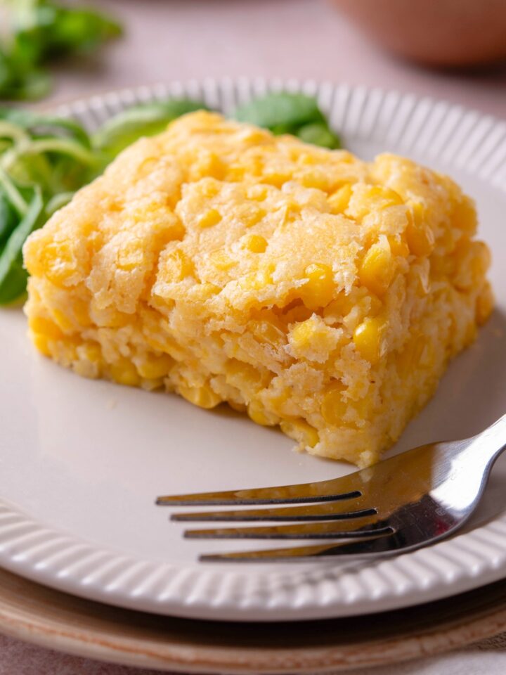 A slice of Jiffy corn casserole on a white plate with a fork on it.