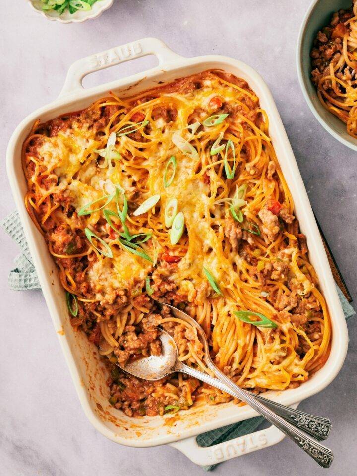 Mexican spaghetti with melted cheese on top in a casserole dish on top of a white counter.