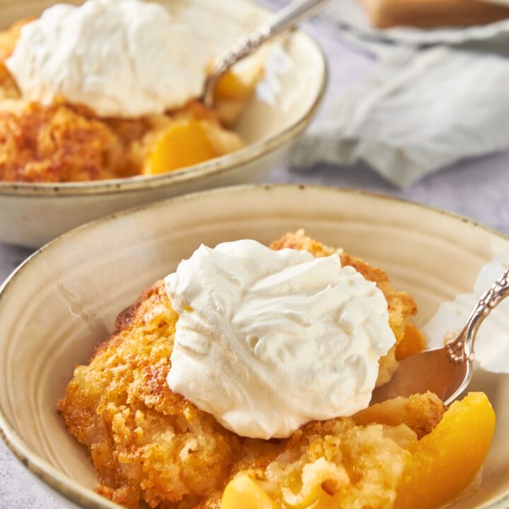 A scoop of vanilla ice cream on top of a peach cobbler with cake mix in a bowl.