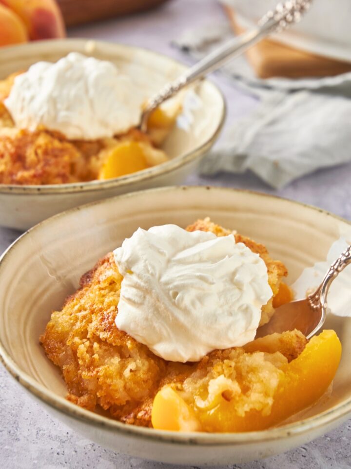 A scoop of vanilla ice cream on top of a peach cobbler with cake mix in a bowl.