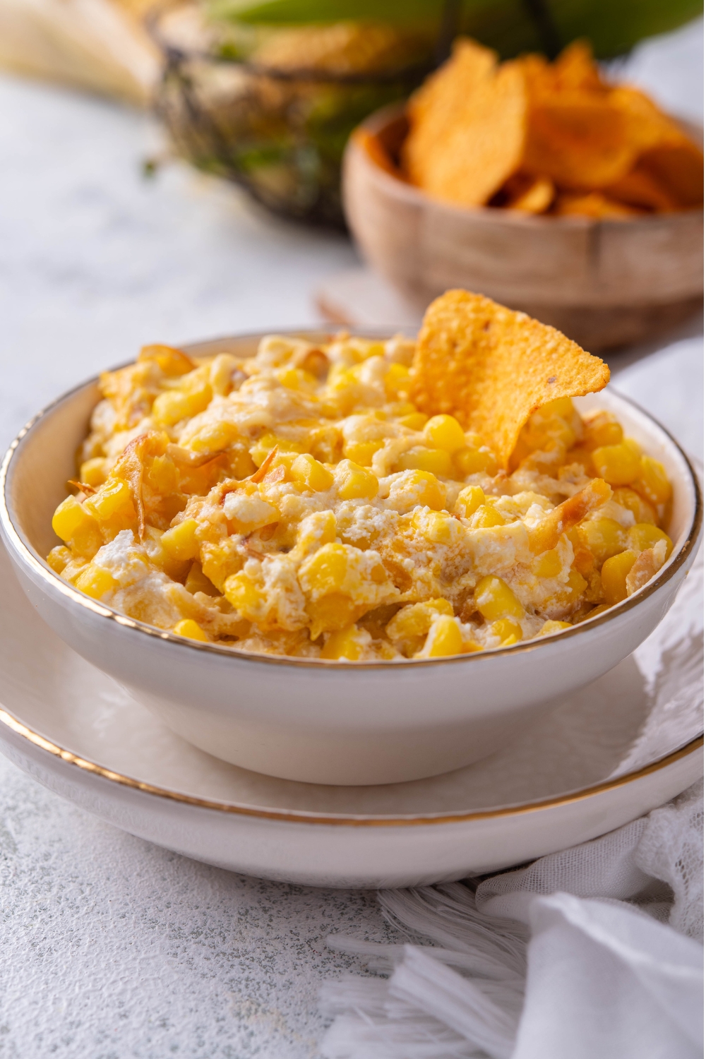 A bowl with corn dip and a tortilla in it. A bowl with extra tortillas is in the background.