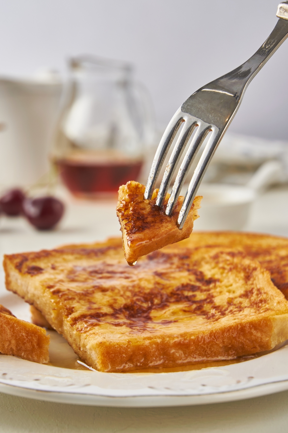 A plate with two slices of french toast and a fork removing a bite of it.