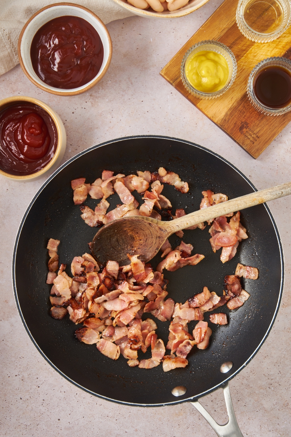 Bacon pieces cooking in a skillet.