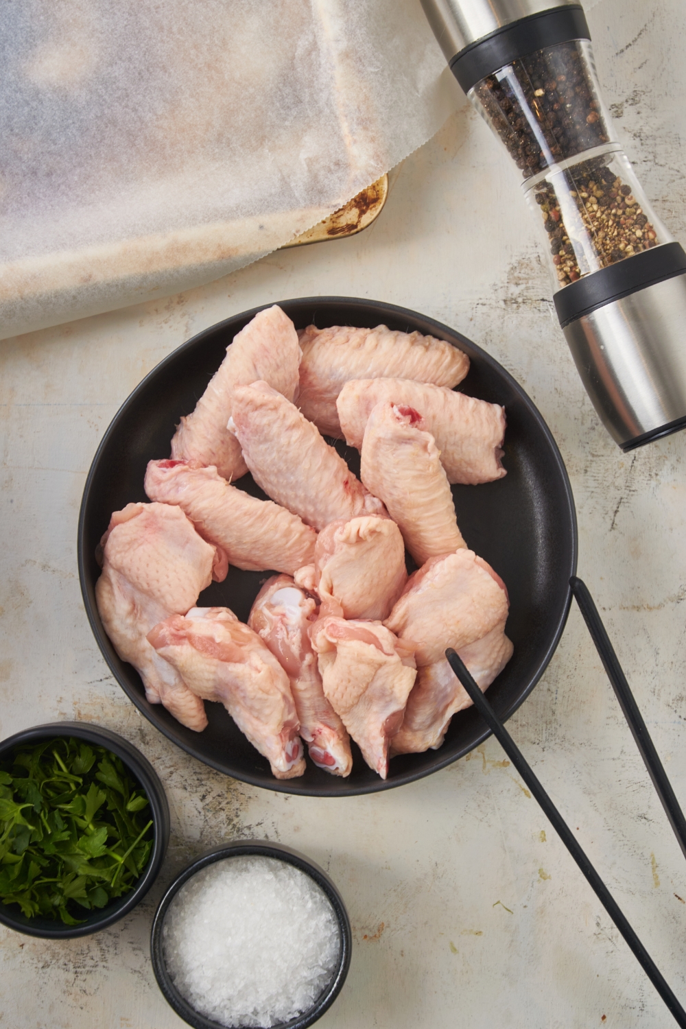 A bunch of uncooked chicken wings in a bowl on top of a white counter.