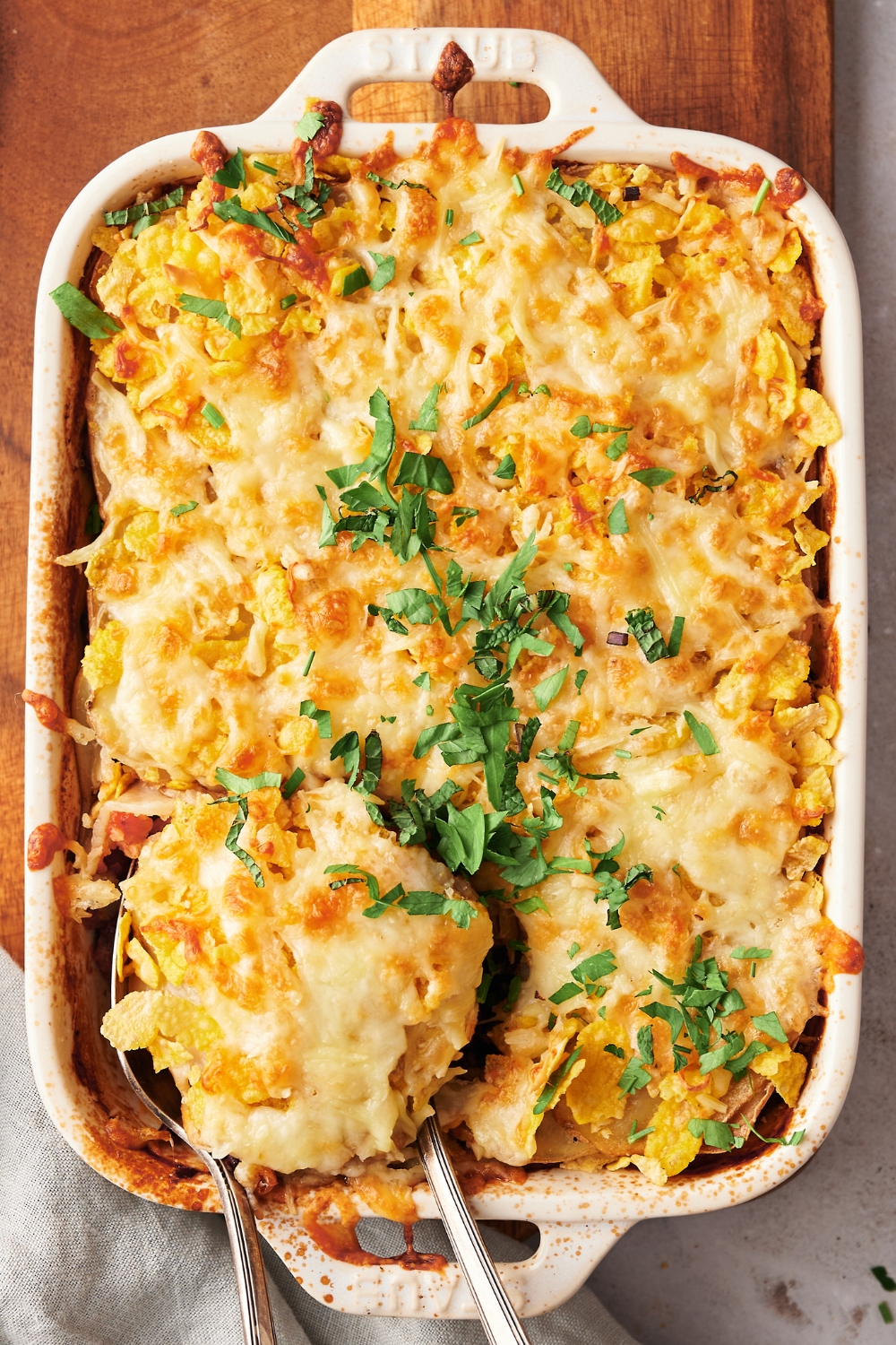 A casserole dish on a wooden serving board with baked shipwreck casserole.