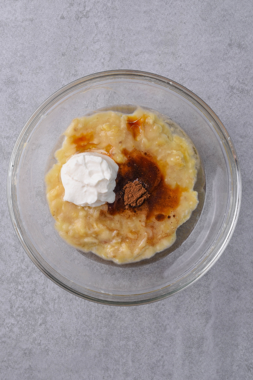 A mixing bowl with mashed banana, vanilla extract, gingerbread spice, oil and sour cream.