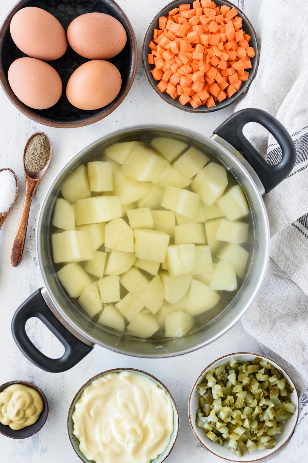 A pot filled with diced and peeled potatoes in water. The pot is surrounded by an assortment of ingredients.