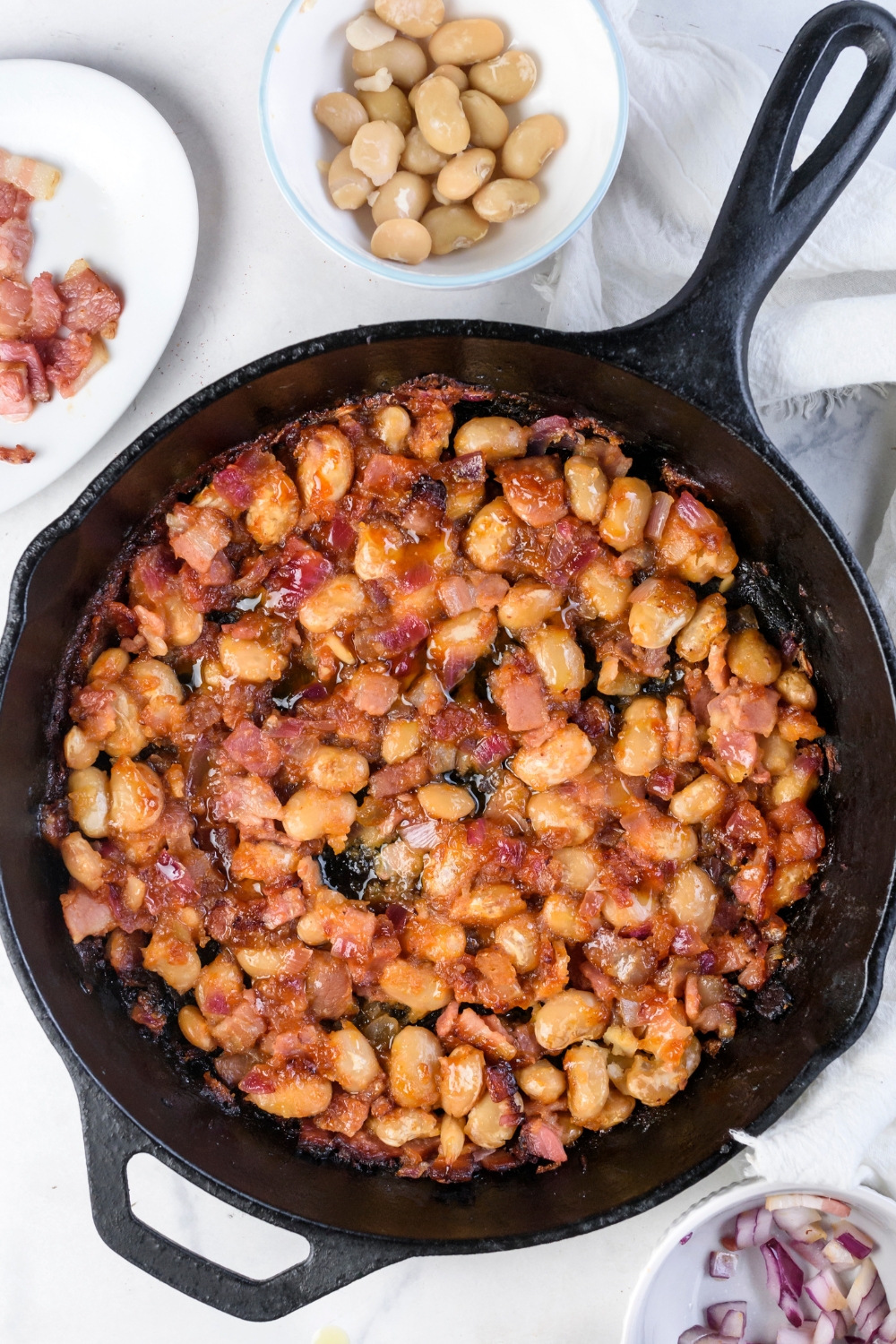 A black skillet filled with fresh baked beans and bacon all coated in a brown sauce.