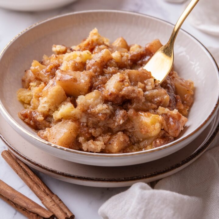 A bowl of caramel apple dump cake with a fork in the bowl and a second bowl of cake in the background.