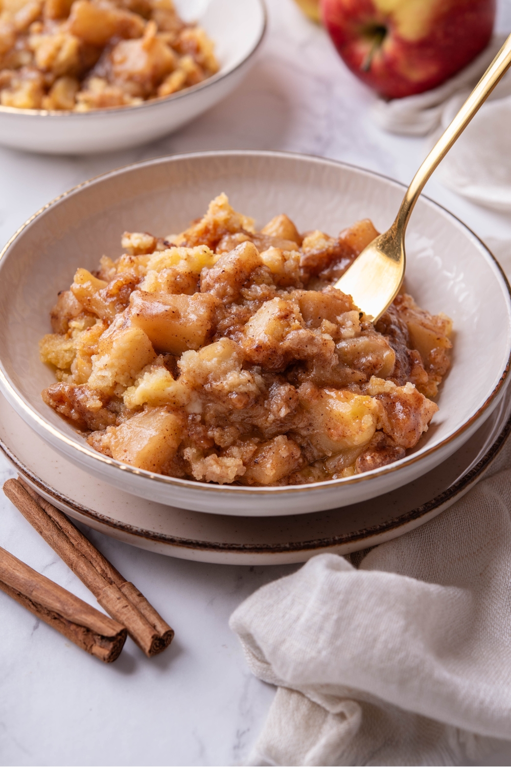 A bowl of caramel apple dump cake with a fork in the bowl and a second bowl of cake in the background.