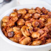 A white bowl filled with baked beans and pieces of crispy bacon coated in sauce.