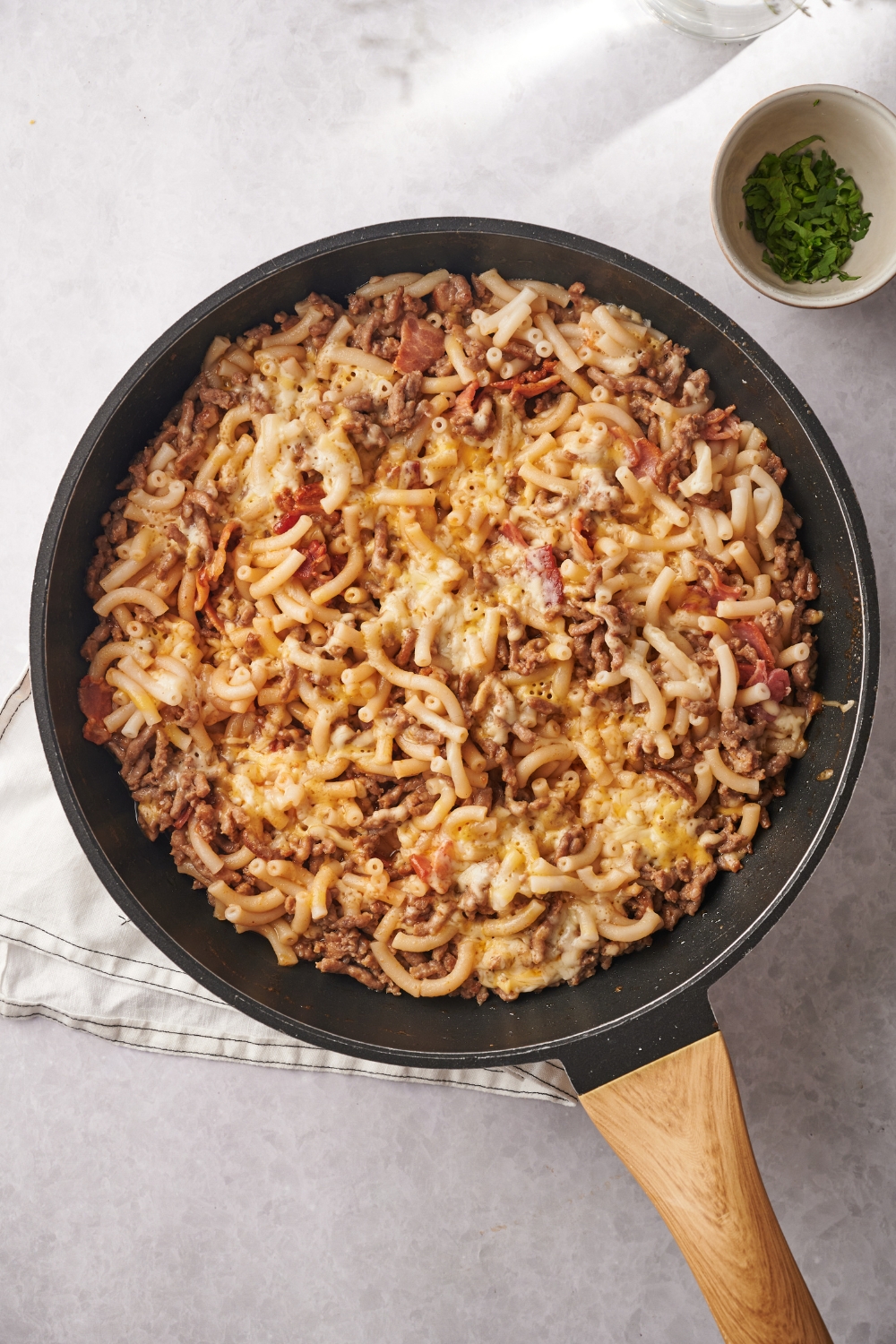 A skillet filled with cooked ground beef, pasta, and bacon covered in a layer of melted cheese.