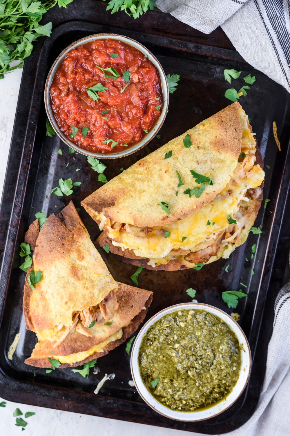 A tray with three crispy tacos stuffed with chicken and melted cheese. One taco is broken in half with each half stacked on top of each other and there are two bowls of red and green salsa on the tray.