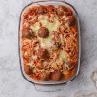 A baking dish filled with freshly baked spaghetti and meatballs in red sauce topped with melted mozzarella cheese.