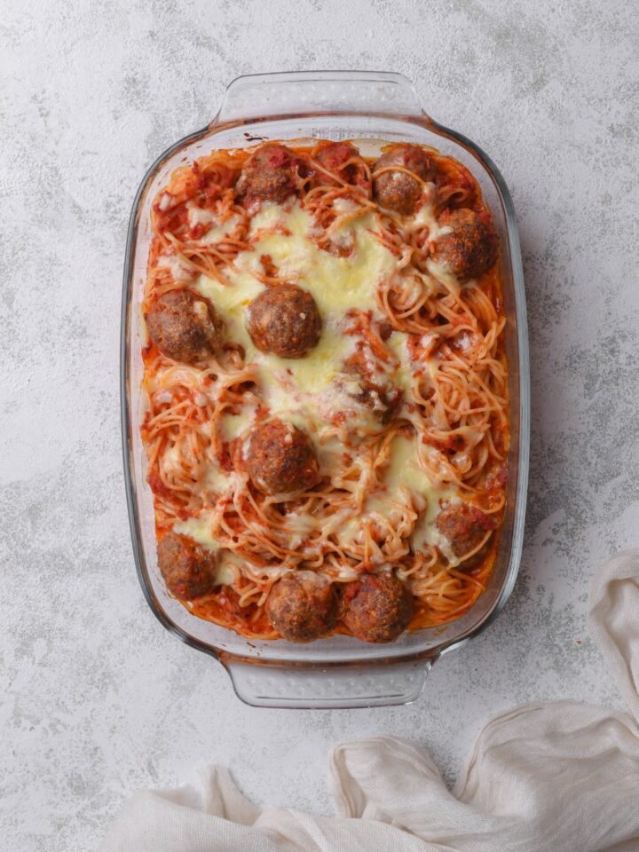 A baking dish filled with freshly baked spaghetti and meatballs in red sauce topped with melted mozzarella cheese.