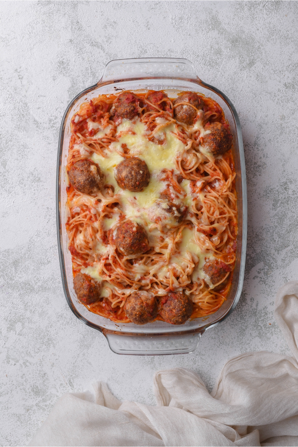 A baking dish filled with freshly baked spaghetti and meatballs in red sauce topped with melted mozzarella cheese.