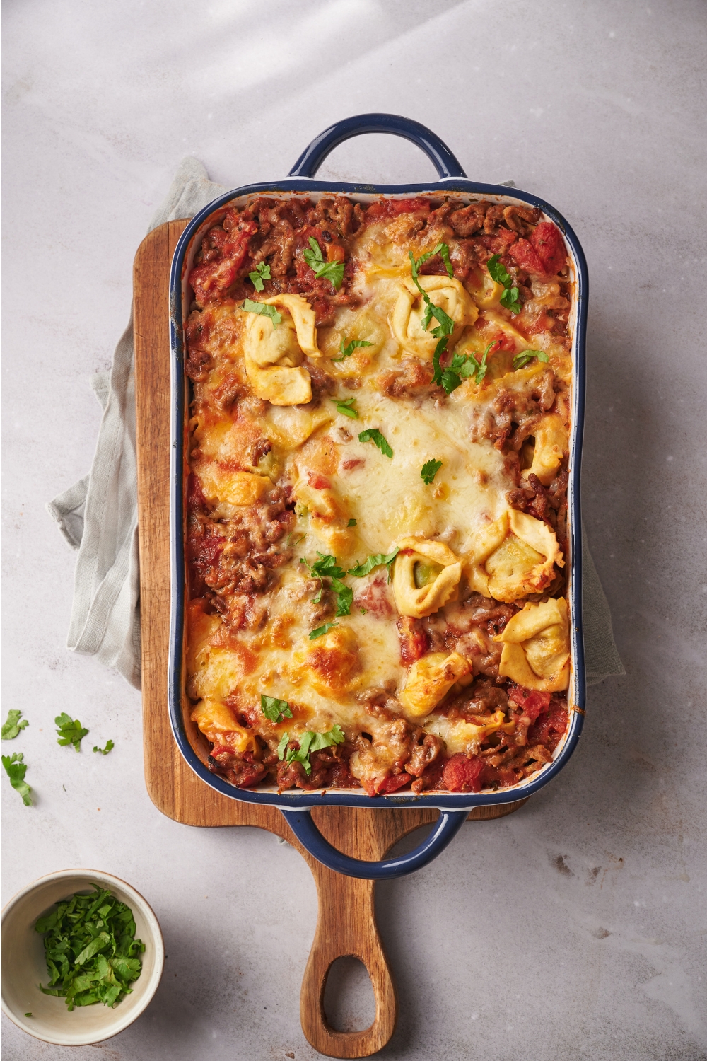 A baking dish filled with freshly baked tortellini casserole covered in melted cheese and garnished with fresh herbs.