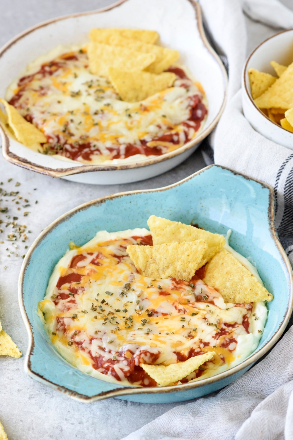 Two baking dishes filled with chili cheese dip covered in a layer of melted cheese with corn chips sticking out of the dip.