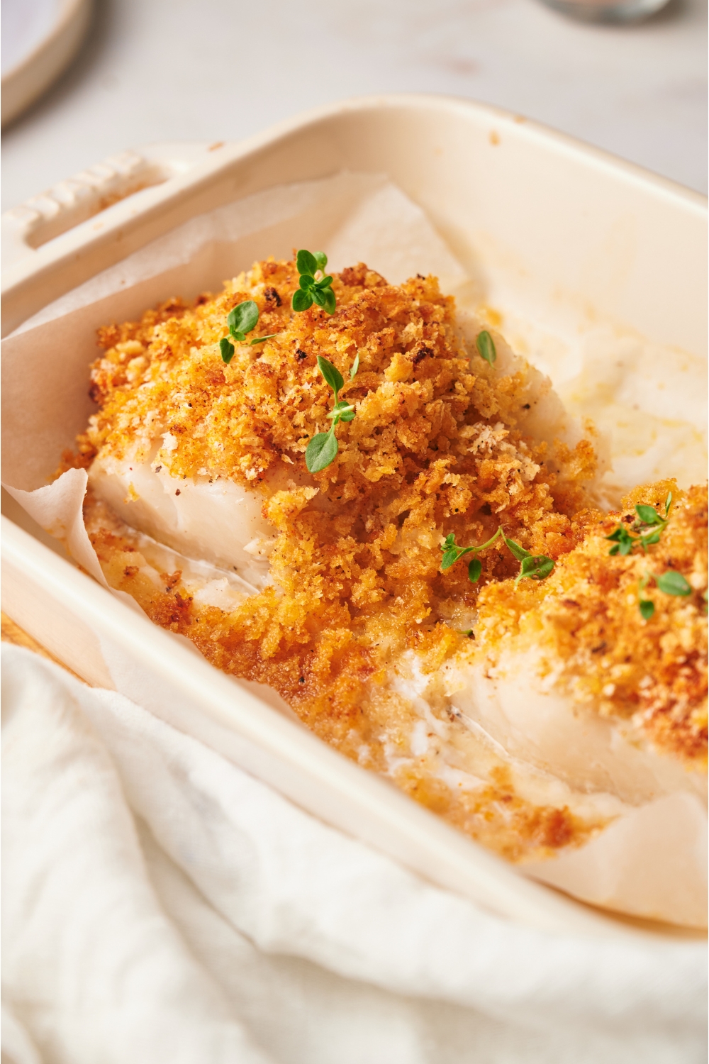 Baked cod topped with a golden brown seasoned crust and garnished with fresh herbs.