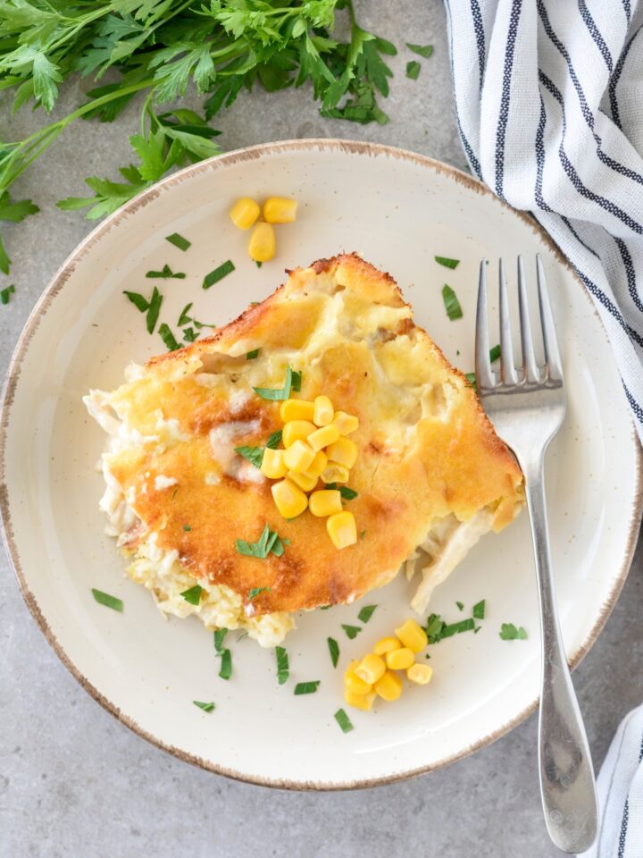 A serving of chicken cornbread casserole topped with whole corn kernels and fresh herbs. There is a fork on the plate.