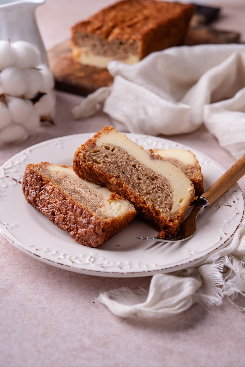 Three slices of cream cheese banana bread overlapping each other with a fork on the plate next to them.