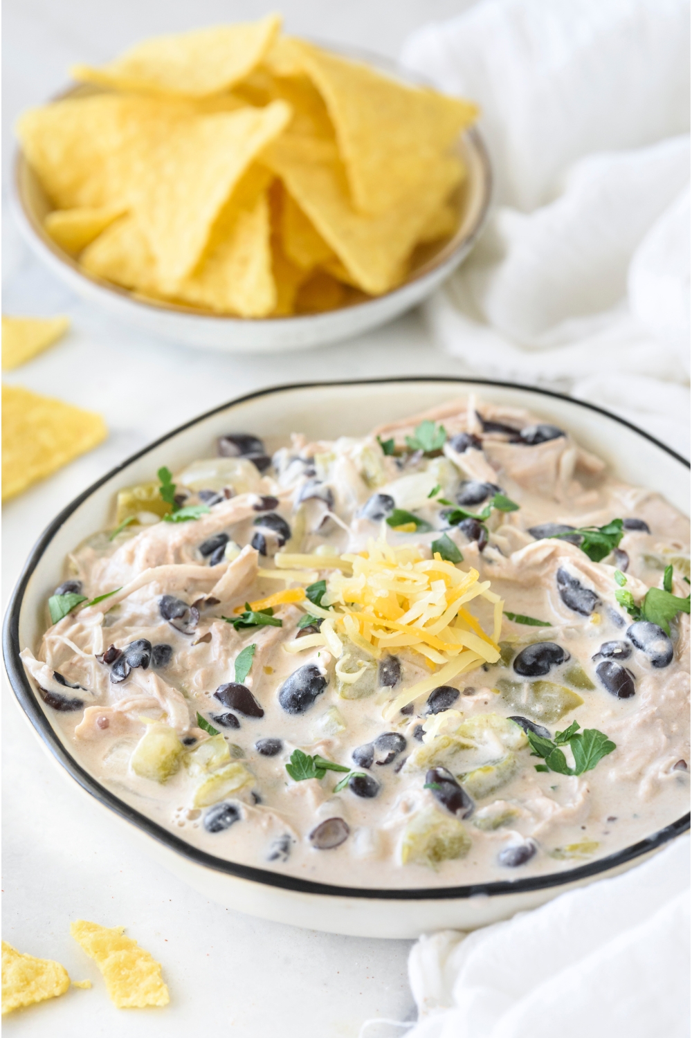 A bowl of white chicken chili with parsley and black beans in the chili and shredded cheese is garnished on top.
