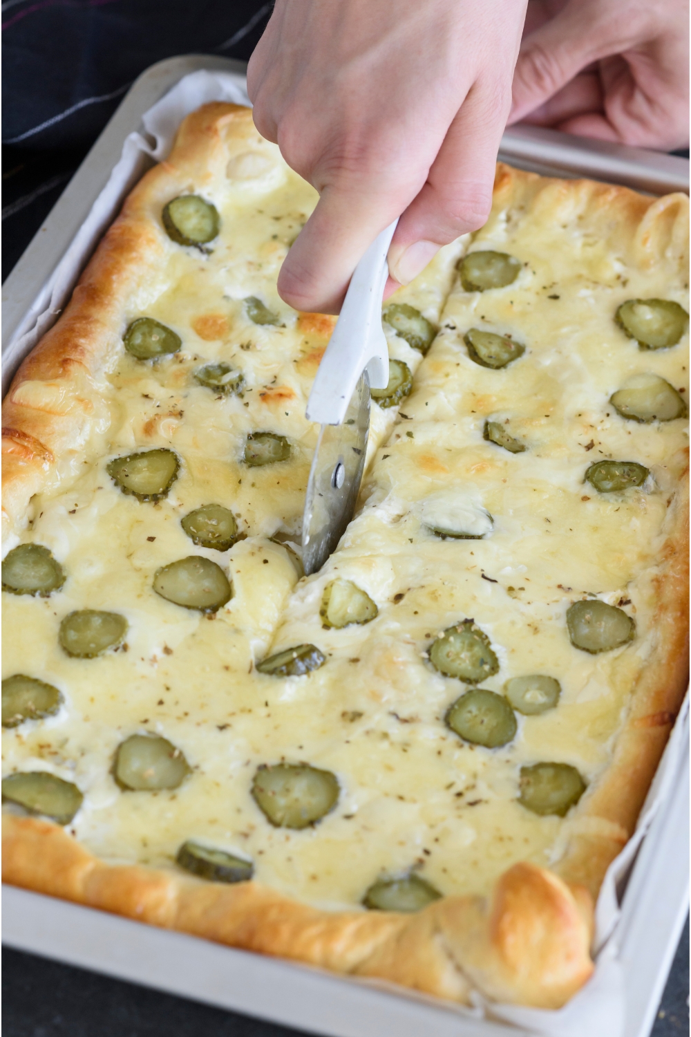 Pickle pizza being sliced using a pizza cutter.