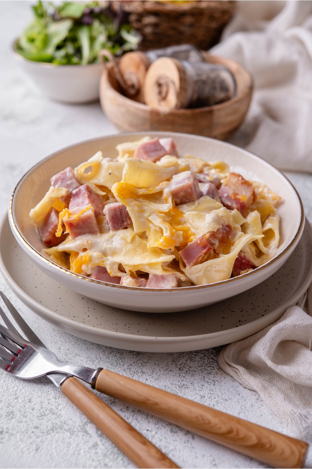 A bowl of ham and noodle casserole atop a plate with two forks next to it.