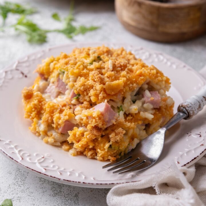 A serving of ham casserole covered in crushed crackers and melted cheese with a fork on the plate.
