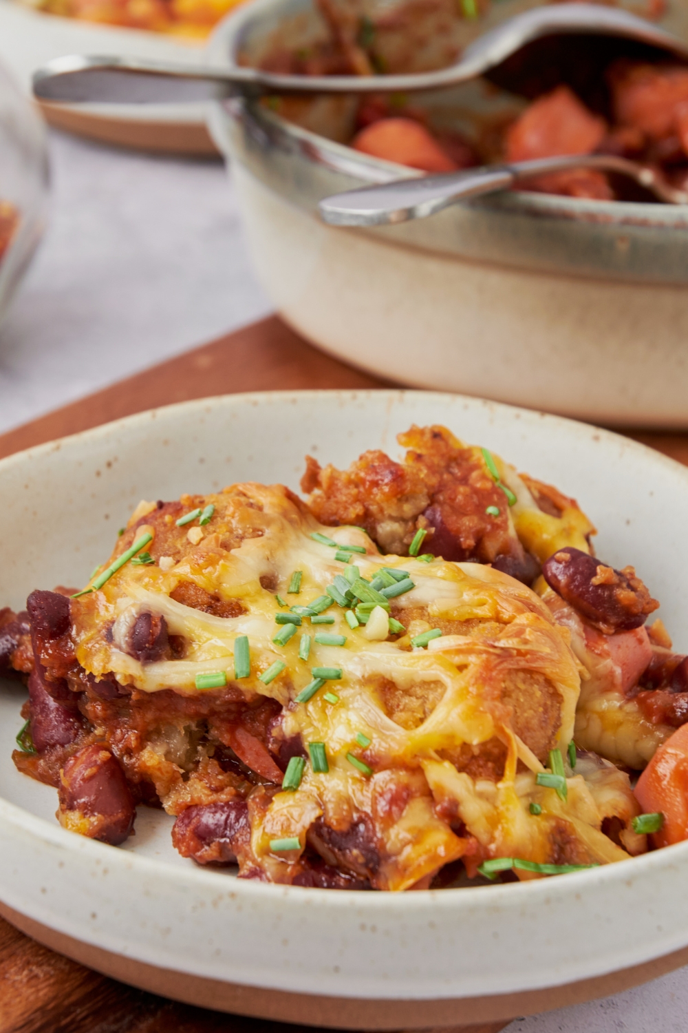 A serving of chili and hot dog casserole with tater tots and melted cheese on top. The casserole is garnished with chives.