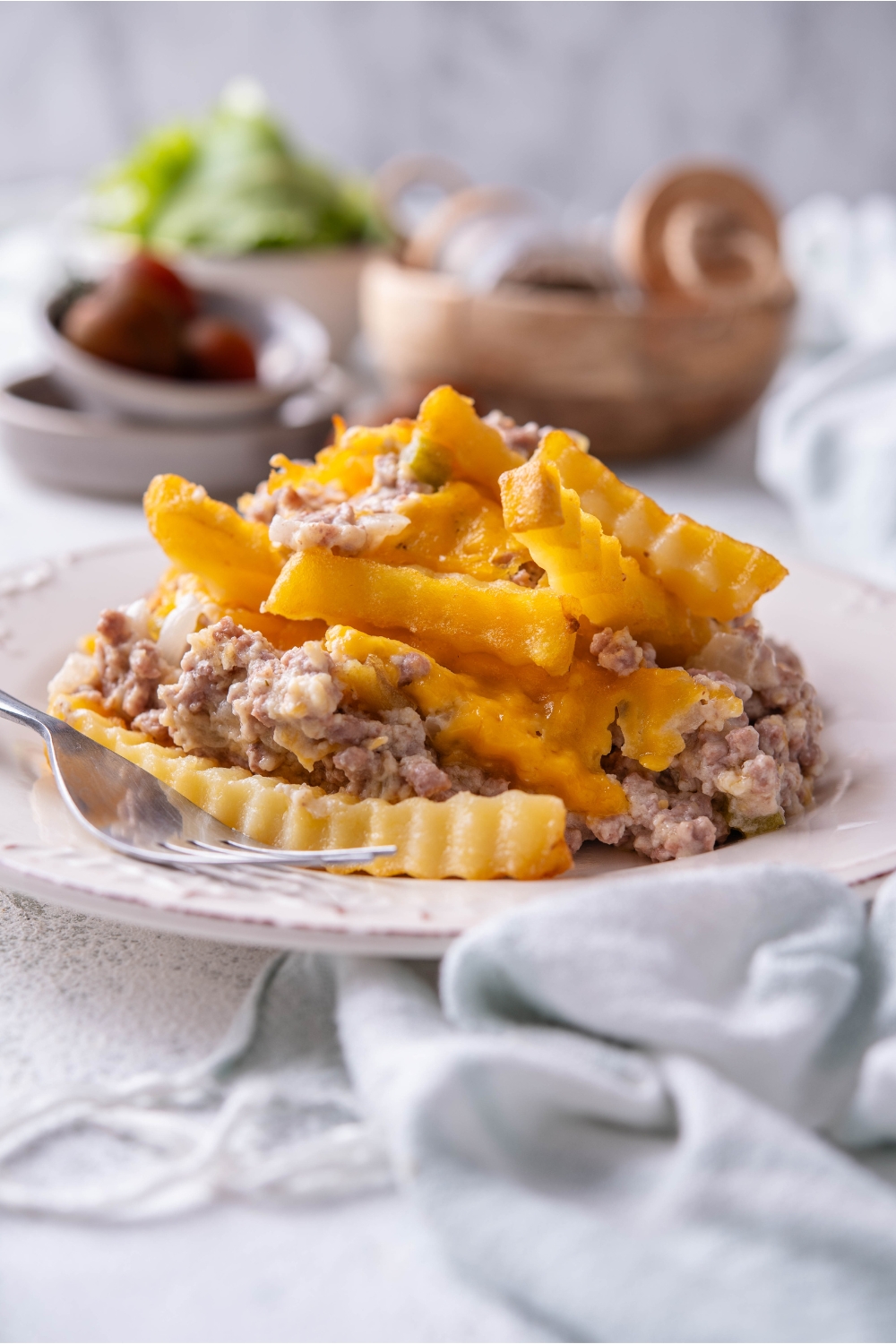 A serving of french fry casserole on a plate piled high with a fork on the plate.