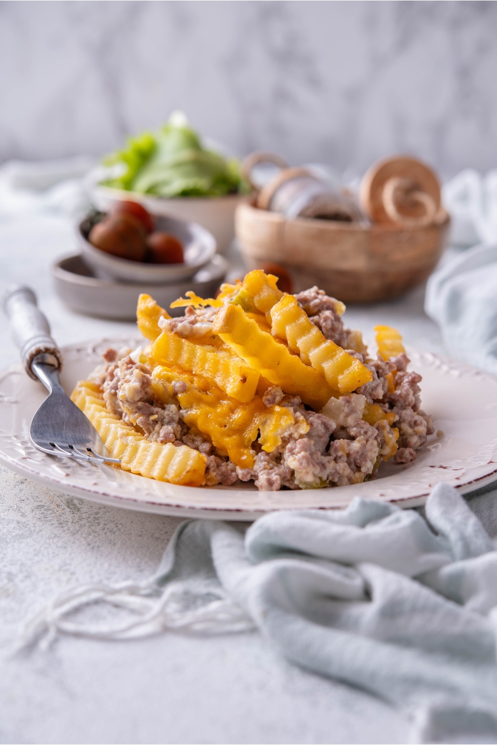 A serving of french fry casserole on a plate piled high with a fork on the plate.