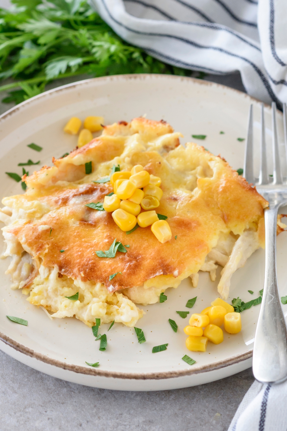 A serving of cornbread chicken casserole topped with fresh corn and green herbs. There is a fork on the plate.