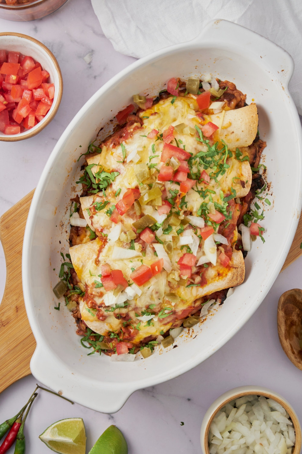 A white baking dish filled with freshly baked casserole covered in diced onion, tomatoes, fresh herbs, and melted cheese.