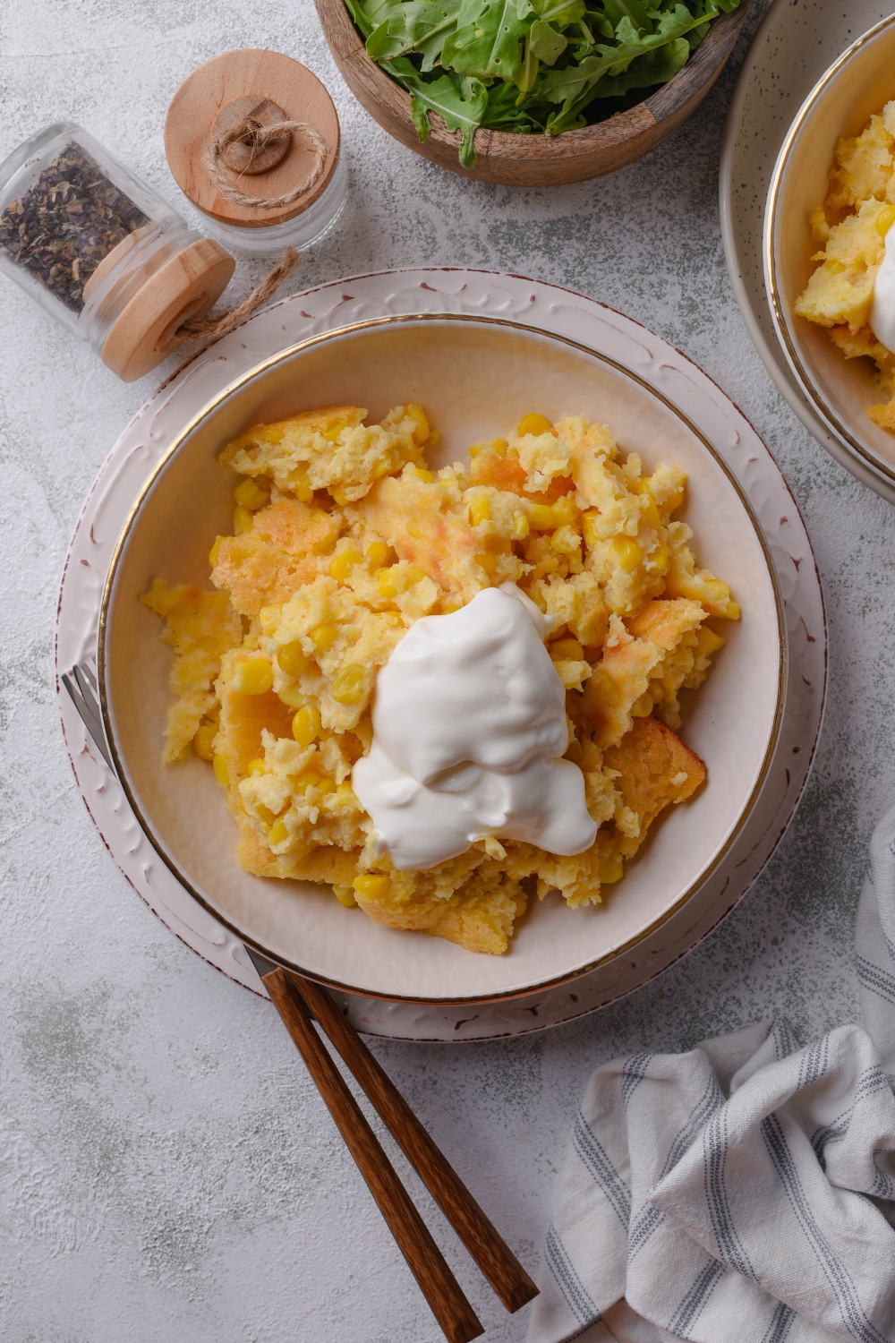 A serving of cornbread pudding in a shallow dish topped with a dollop of sour cream.