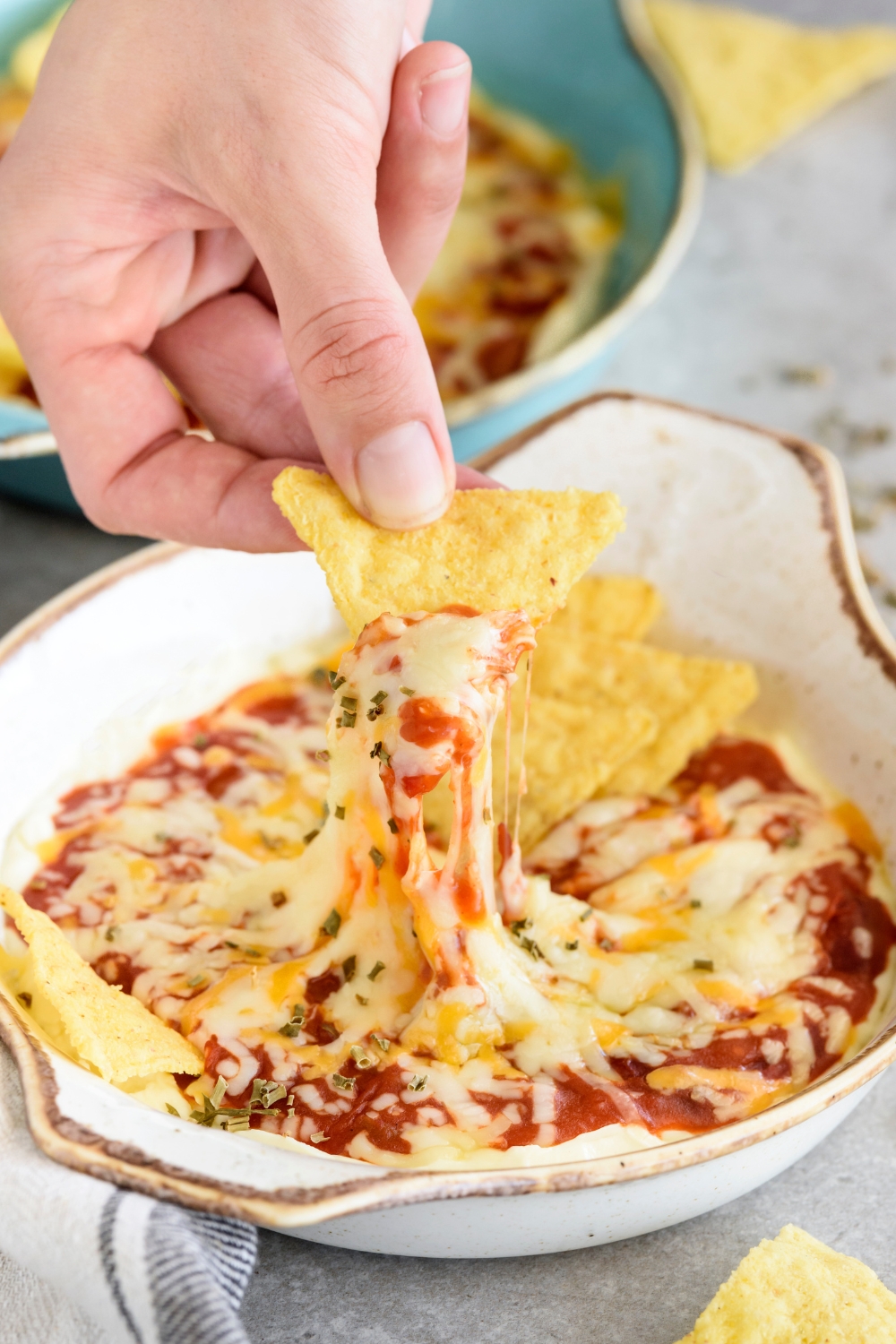 A hand scooping chili cheese dip using a corn chip.