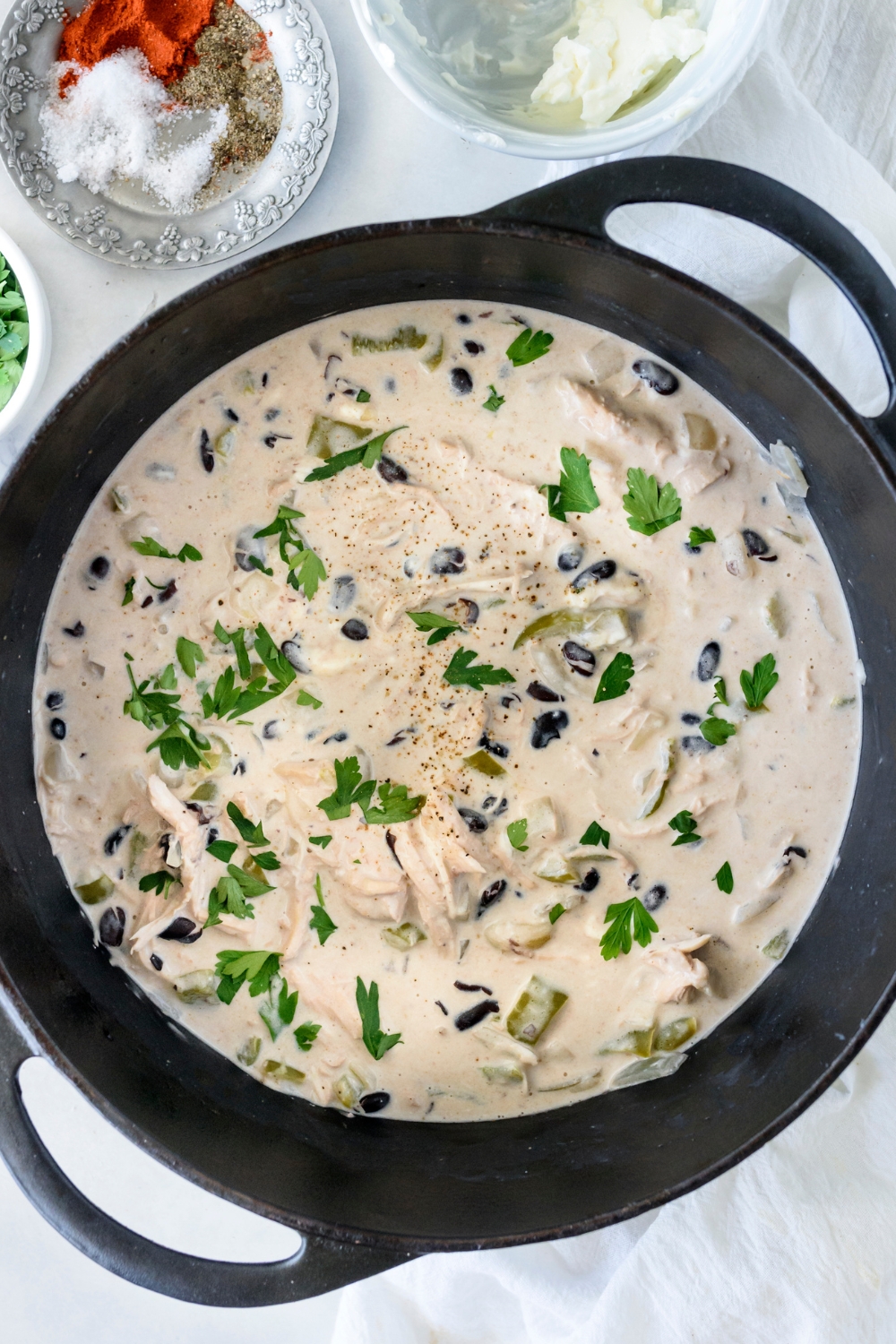A black pot filled with white chicken chili with parsley on top and black beans floating in the chili.
