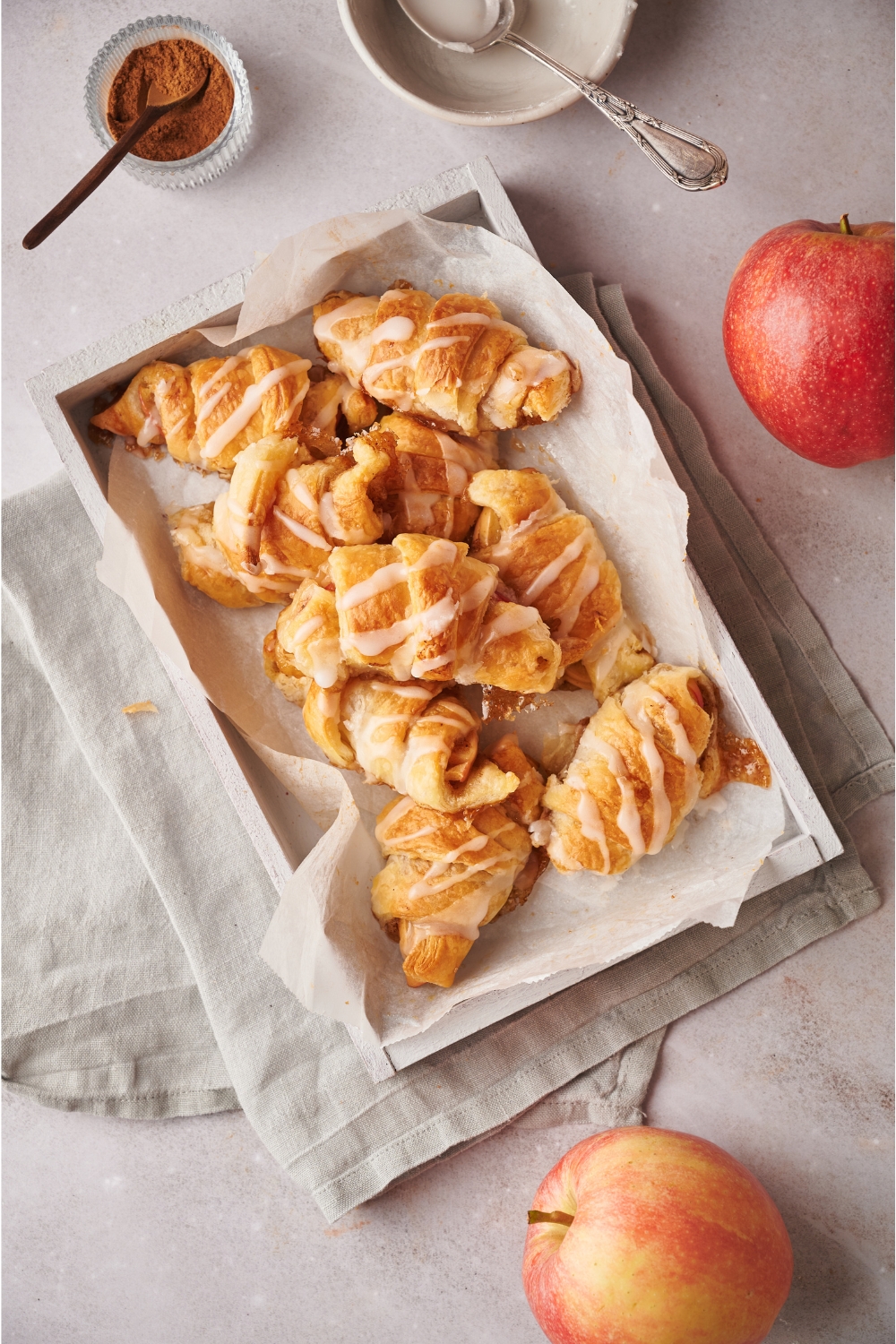 A platter lined with parchment paper filled with crescent roll apple turnovers covered in a sugar glaze.