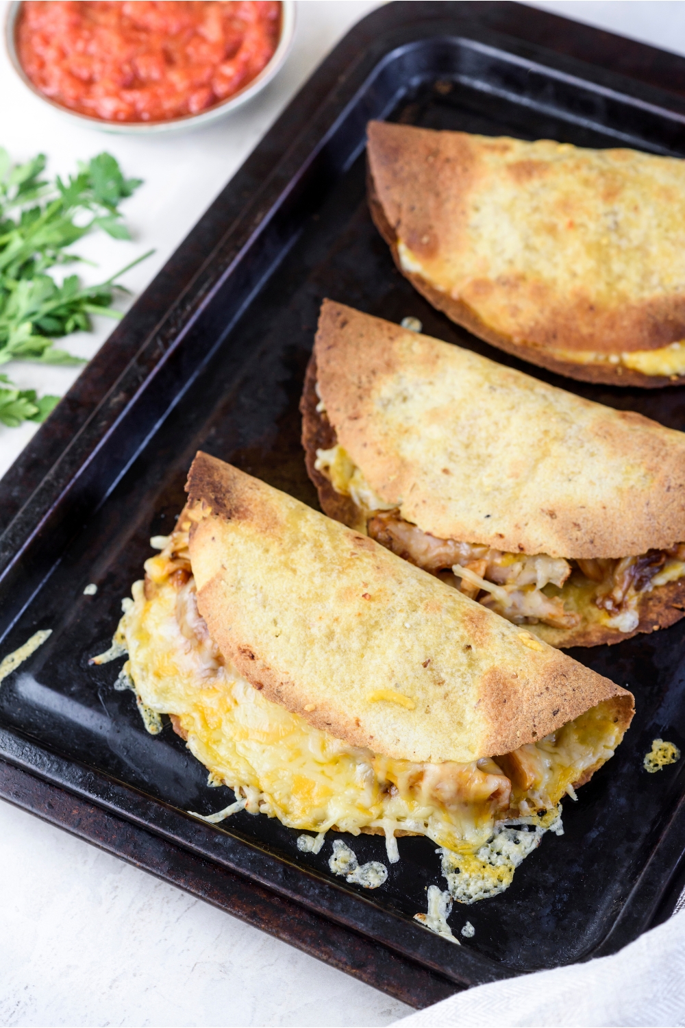 Three crispy tortillas on a baking sheet stuffed with meat and melted cheese.