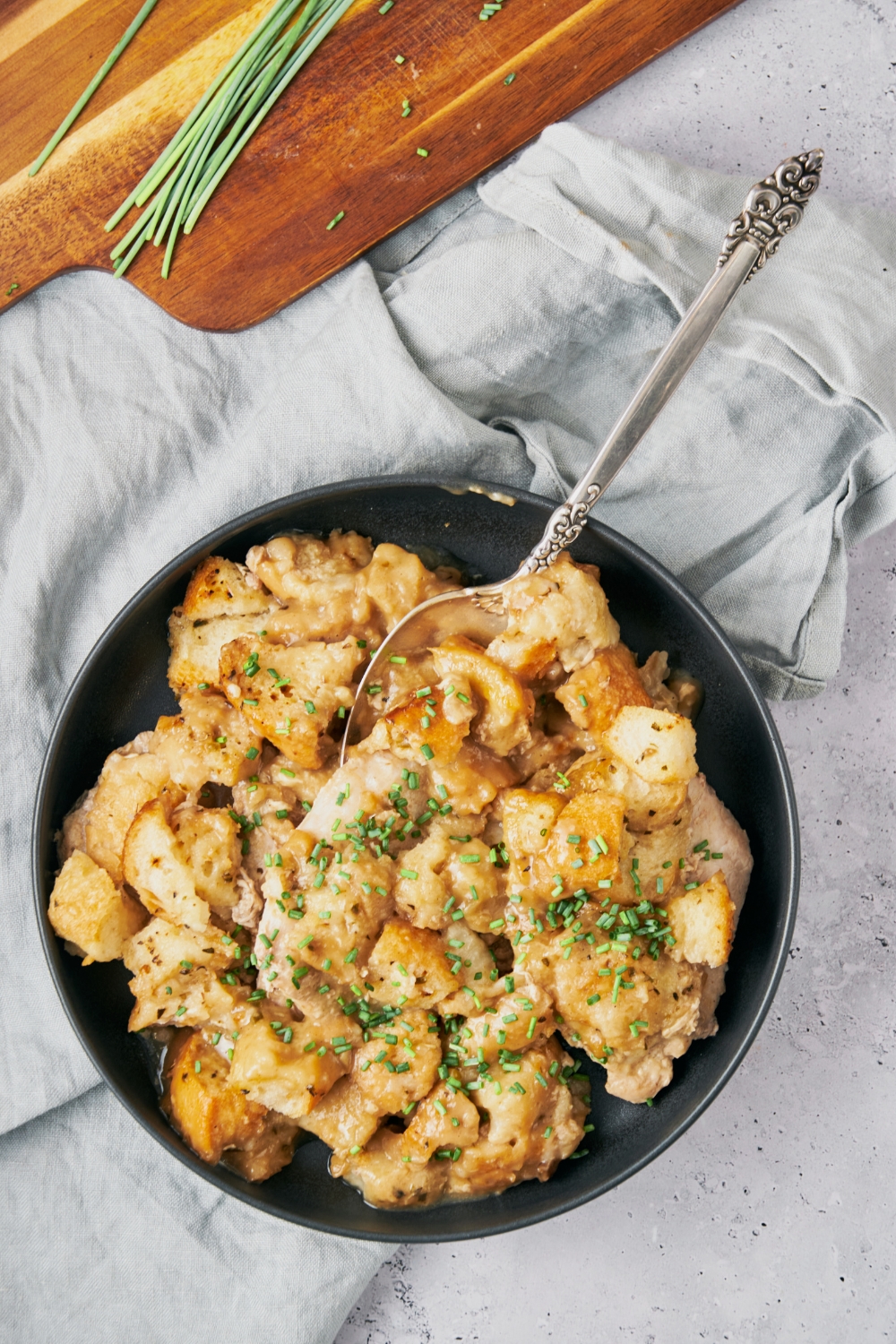 A bowl of slow cooked pork chops covered in stuffing and garnished with chives. There is a spoon in the bowl.