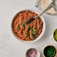 A bowl of taco meat garnished with fresh parsley with two spoons in the bowl.